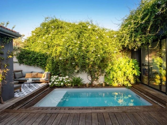 Petite piscine enterrée avec terrasse en bois et jardin fleuri